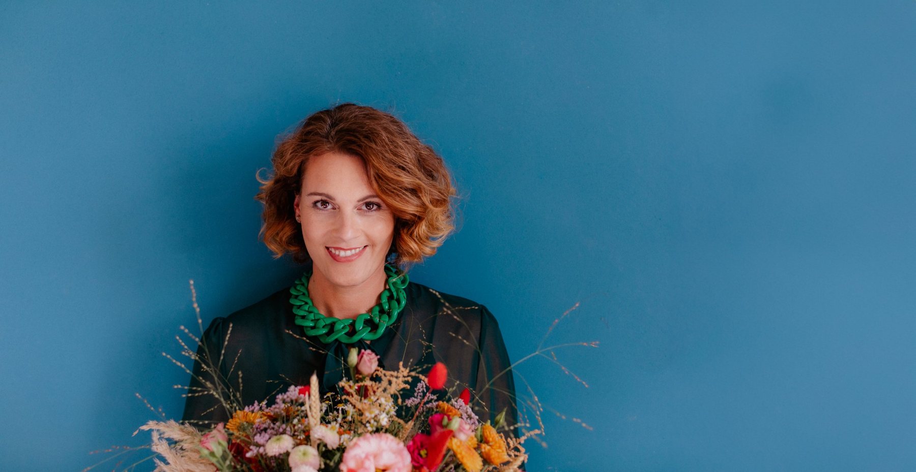Verena Pahmeier mit einem bunten Blumenstrauß vor einer blauen Wand